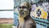 image of Aboriginal man standing in front of buildling painted with art