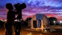 sunset image with woman looking through telescope and couple sitting in front of dome