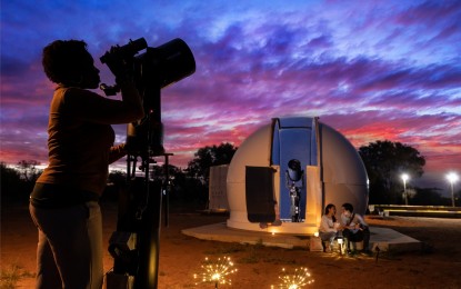 sunset image with woman looking through telescope and couple sitting in front of dome