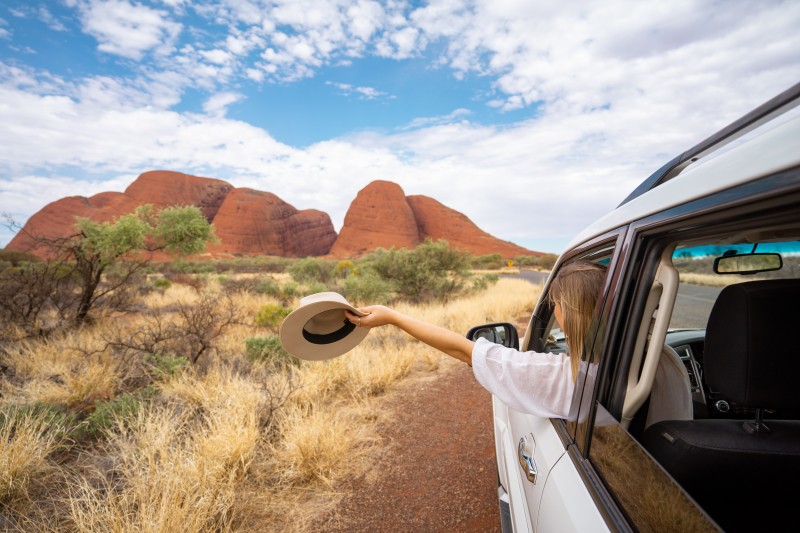 image of woman holding hat out window as driving towards red boulders
